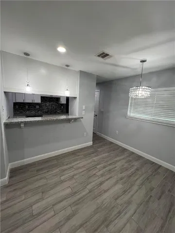 an empty room with wooden floor and kitchen view