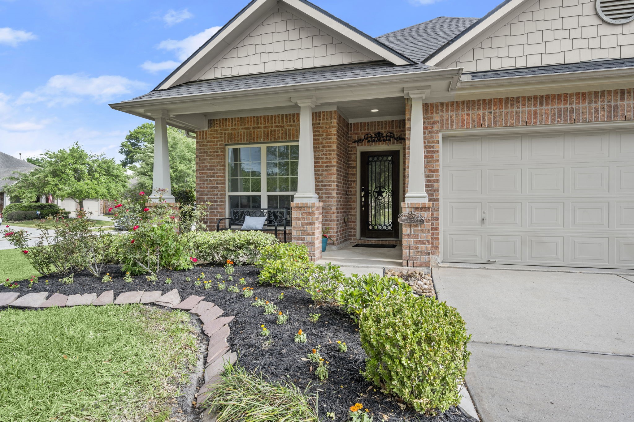 This charming home features a welcoming front porch with brick accents and elegant columns. The well-maintained garden and landscaping add curb appeal, while the attached garage provides convenience. Perfect for a cozy and inviting entrance.