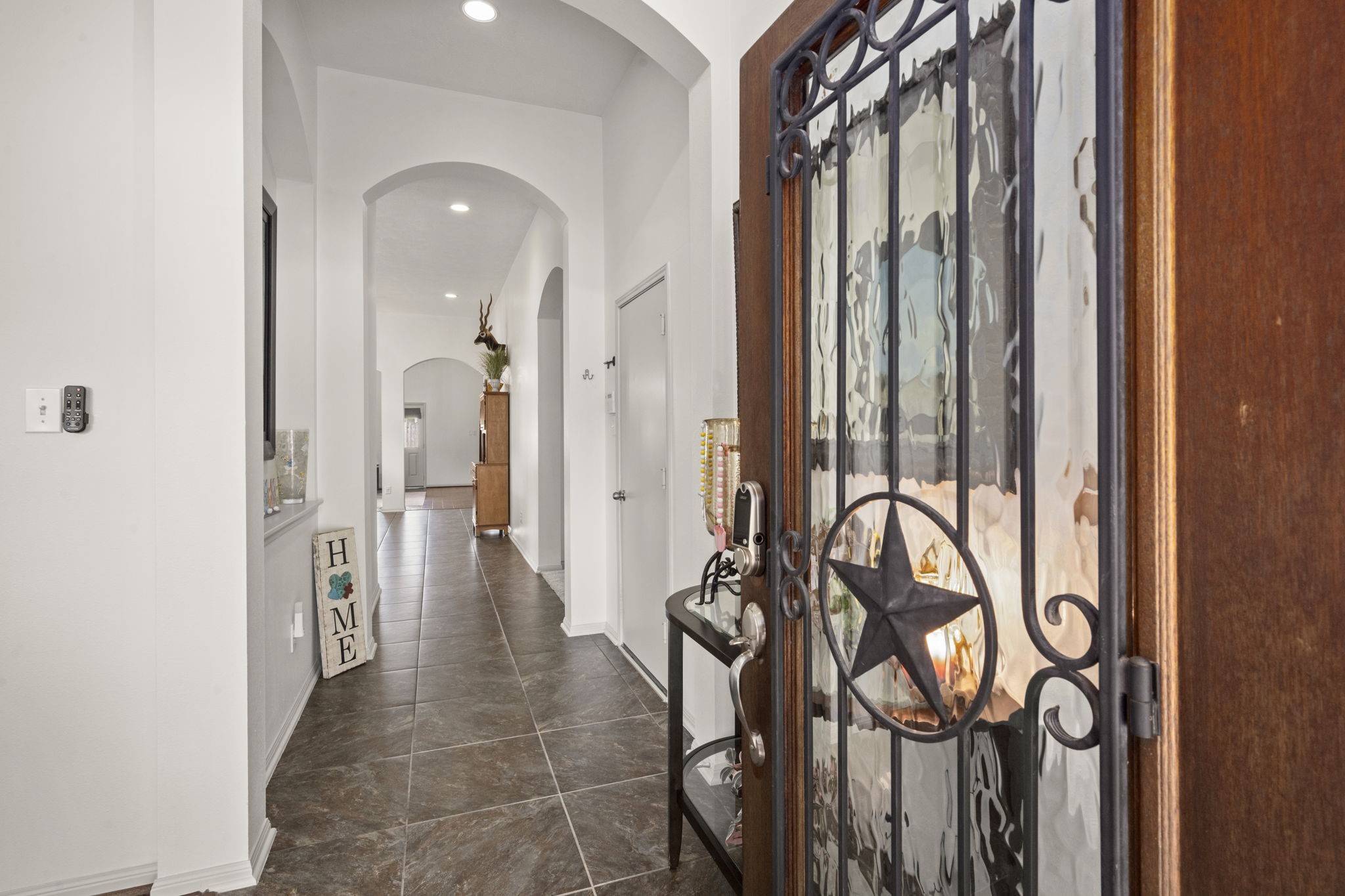 27526 Gatlin Lane Spring, TX 77386 - Photo 2 of 31 Welcoming entryway with a decorative wooden door featuring a star design. The hallway is spacious and well-lit, with arched doorways and polished tile floors leading into the home.