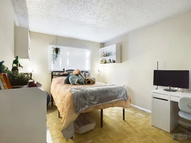 a bedroom with a bed and a computer on the desk next to a window