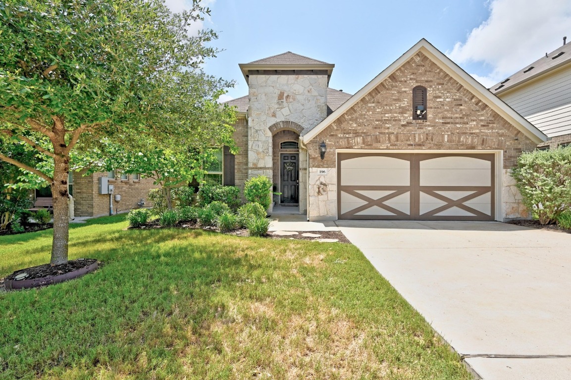 French provincial home with a garage, stone siding, a front lawn, concrete driveway, and brick siding