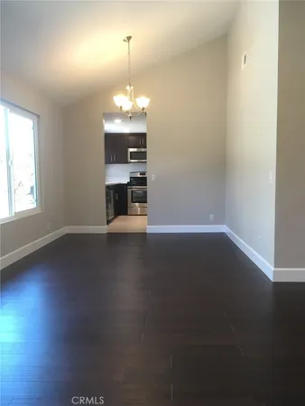 an empty room with wooden floor chandelier and windows