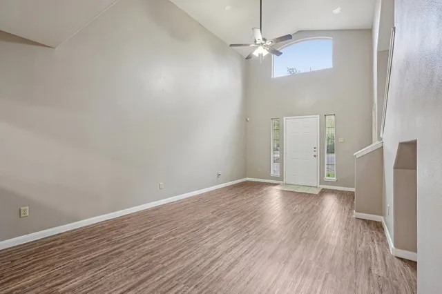 an empty room with wooden floor fan and windows