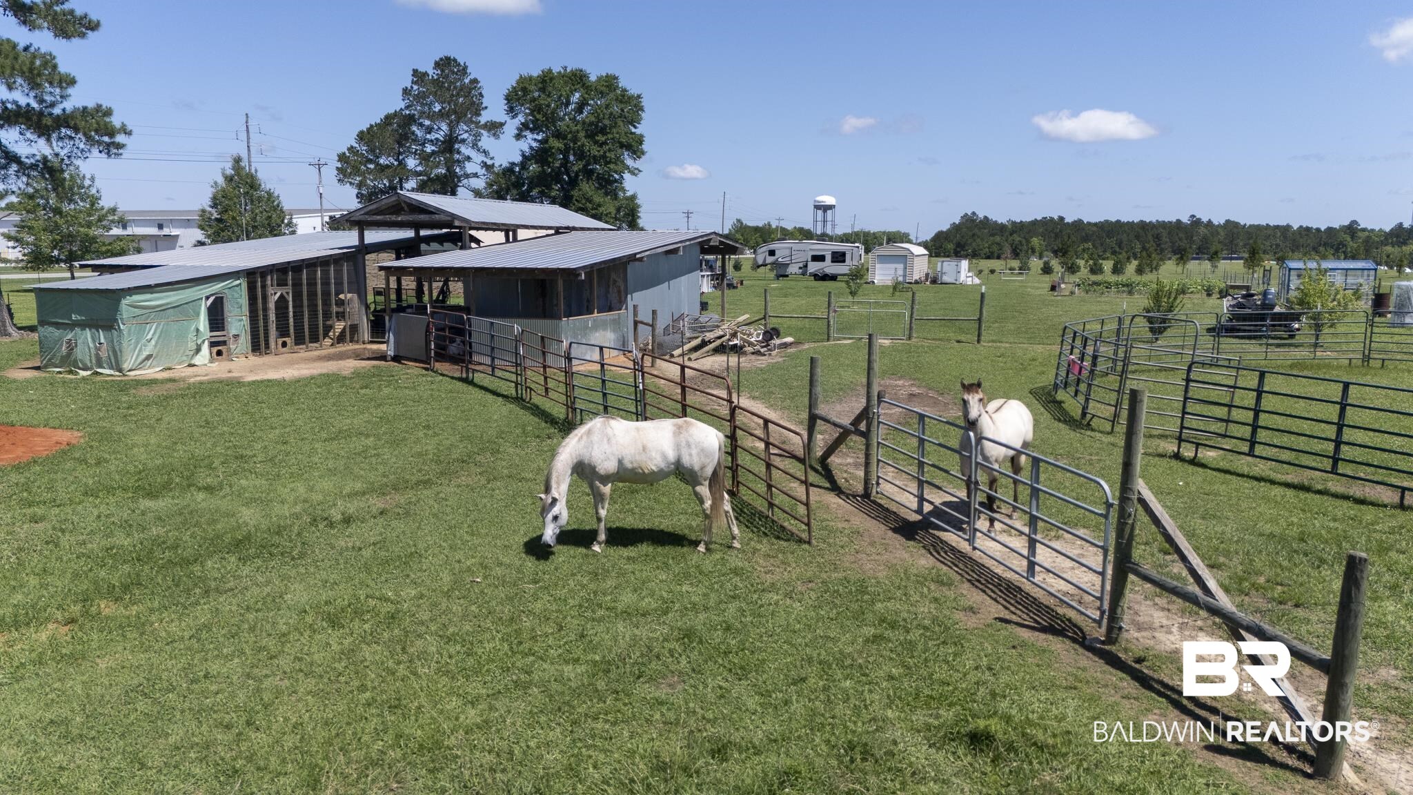 30580 County Road 49 Loxley, AL 36551 - Photo 28 of 32 Expansive green pasture with multiple metal-roofed outbuildings, fenced enclosures, and a dirt path