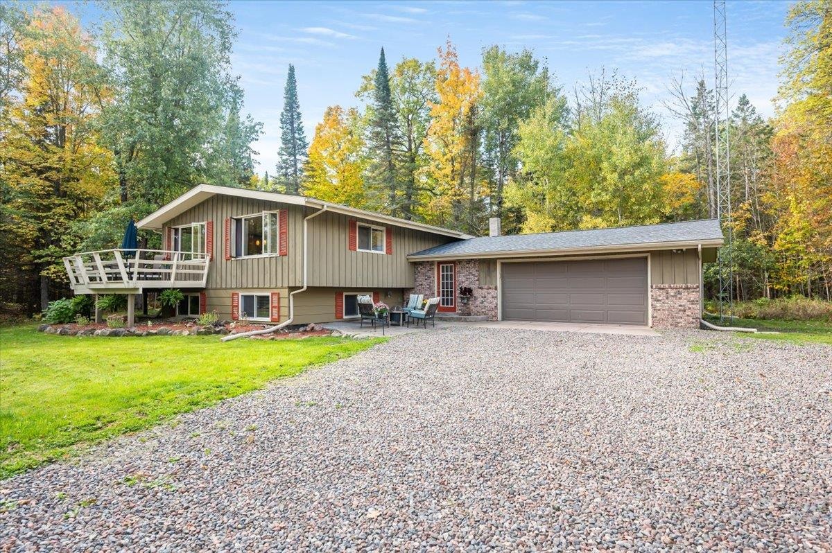 6891 South Oakland Road Superior, WI 54880 - Photo 1 of 29 Tri-level home featuring a front lawn, gravel driveway, a patio area, an attached garage, and board and batten siding