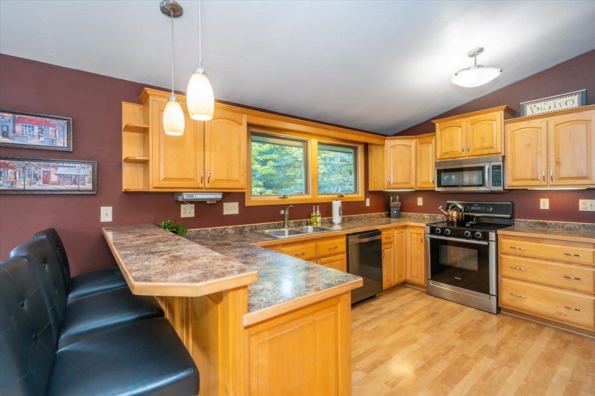 6891 South Oakland Road Superior, WI 54880 - Photo 4 of 29 Kitchen featuring stainless steel appliances, lofted ceiling, dark countertops, hanging light fixtures, and light wood-type flooring