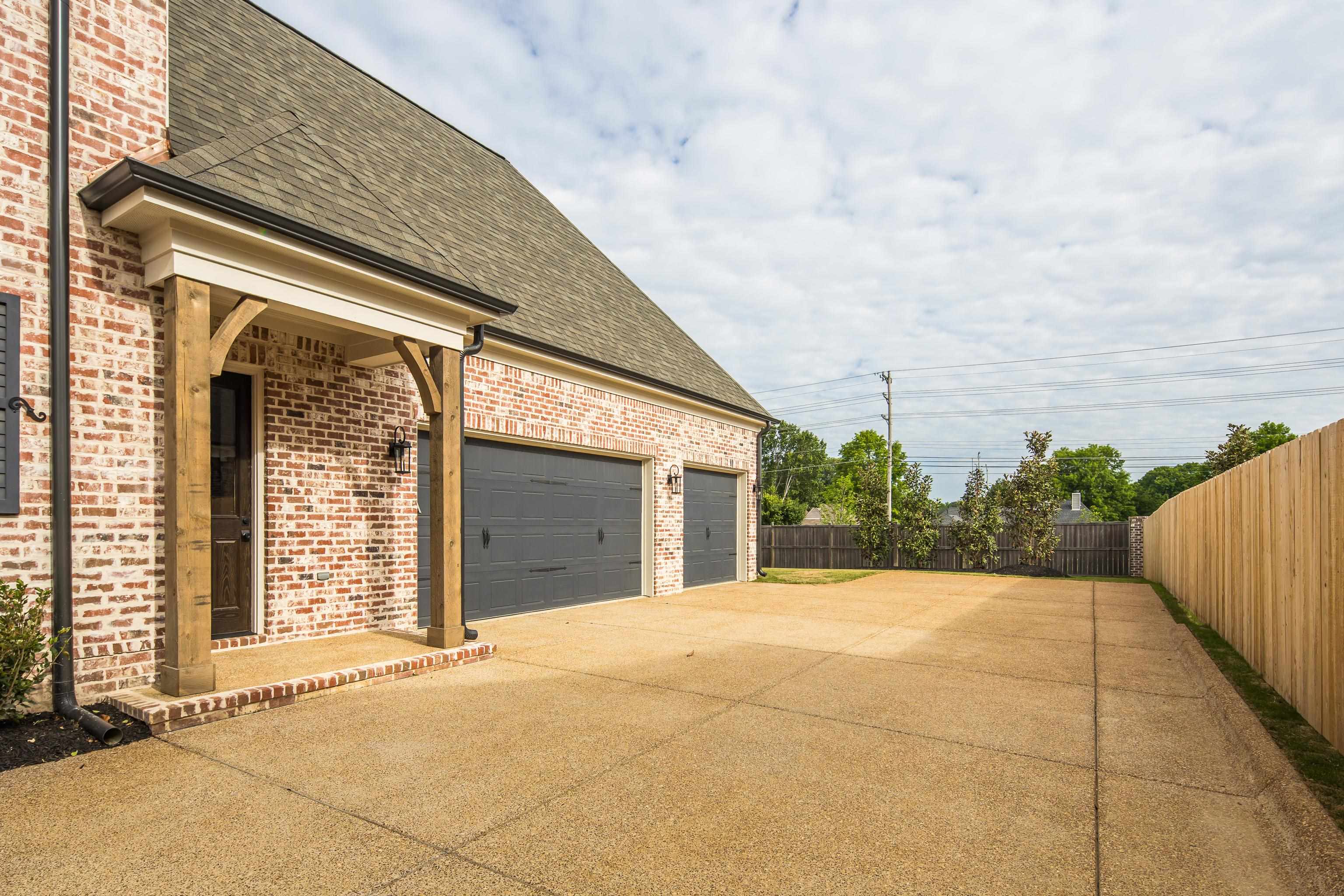 284 Keisie Lane Collierville, TN 38017 - Photo 2 of 34 Exterior showcasing a light brick facade with a two-car garage, covered entry with timber frame accents, dark asphalt shingle roof, and an expansive concrete driveway