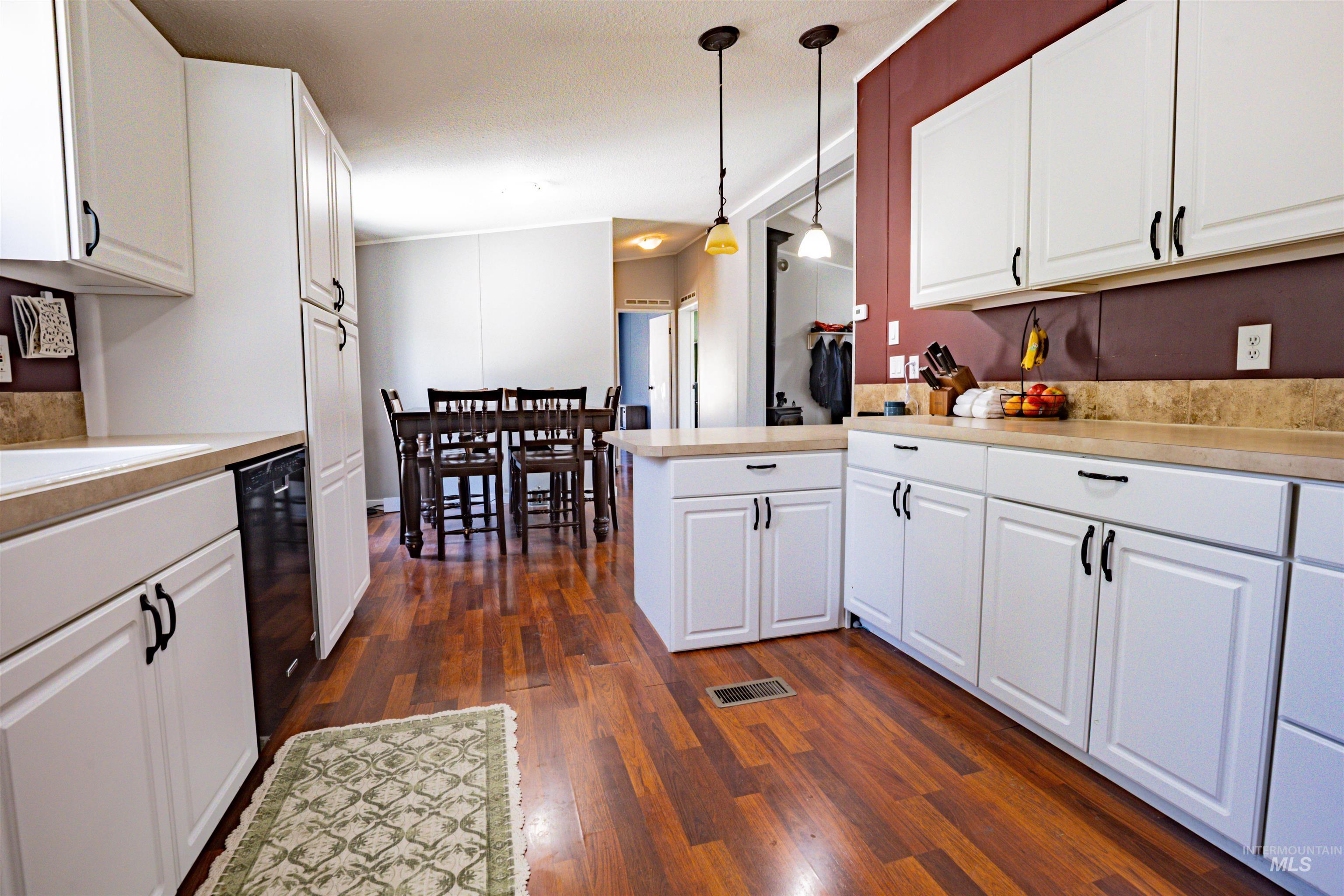 23904 Southview Lane Middleton, ID 83644 - Photo 24 of 29 Kitchen featuring wood-finish flooring, white cabinetry with black hardware, light-toned countertops, and a full-size dishwasher