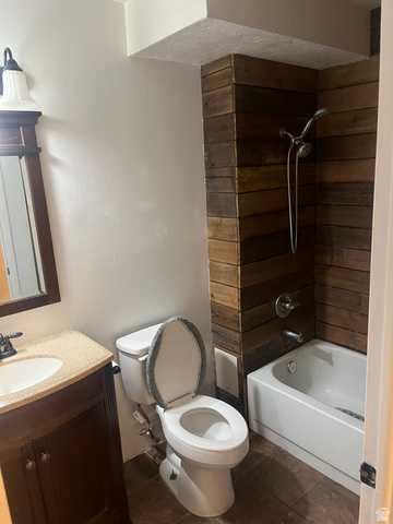 1175 Canyon Road, Unit A 5 Ogden, UT 84404 - Photo 13 of 15 Bathroom featuring a wood-panel accent wall, white bathtub with a chrome shower fixture, and a dark wood-finish vanity with a light-toned countertop and integrated sink