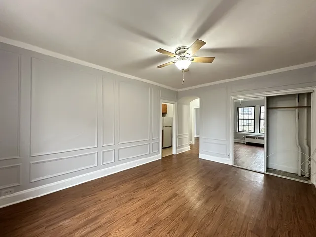 an empty room with wooden floor chandelier fan and windows