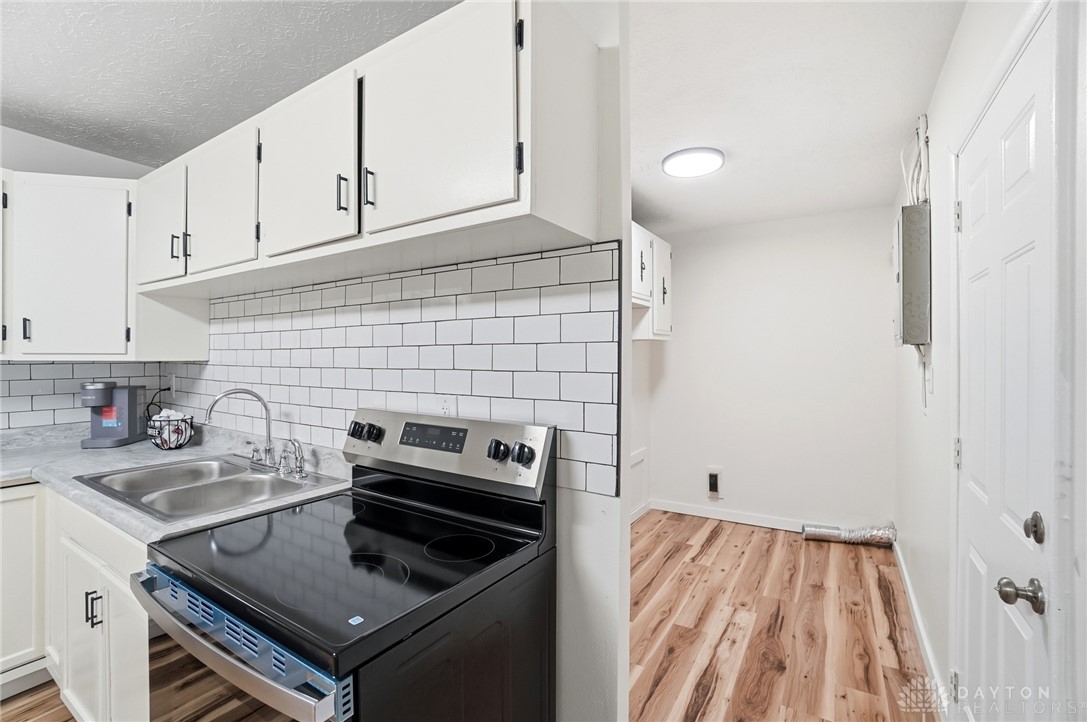 1923 Portage Path Springfield, OH 45506 - Photo 18 of 40 A compact kitchen with sleek appliances and practical cabinetry transitions to an adjacent utility space, all adorned with warm wood flooring.