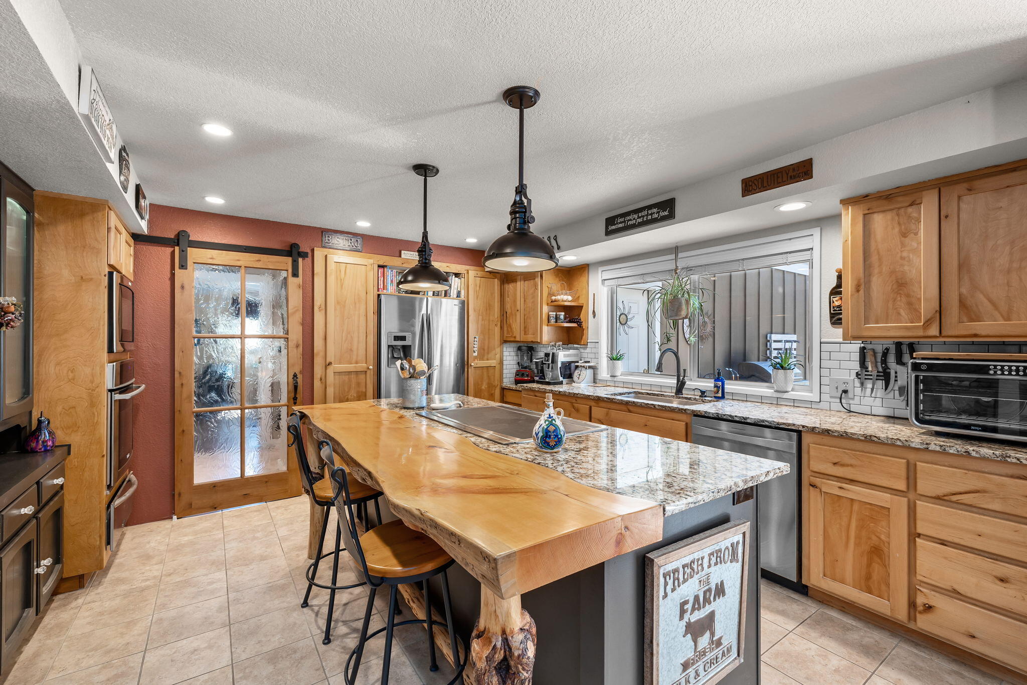 21870 Rincon Avenue Bend, OR 97702 - Photo 8 of 47 . Rustic charm of custom log post banister accents, gliding barn door and juniper & granite breakfast bar blends perfectly w/well equipped kitchen that inc. wine fridge and warming drawer.