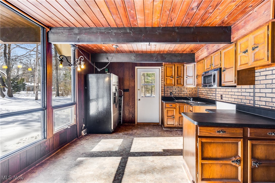 Kitchen with dark countertops, wood finish cabinetry, stainless steel appliances, a wood ceiling with exposed beams, and a peninsula