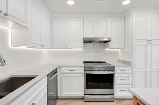 a large kitchen with kitchen island a sink a stove a refrigerator and white cabinets with wooden floor