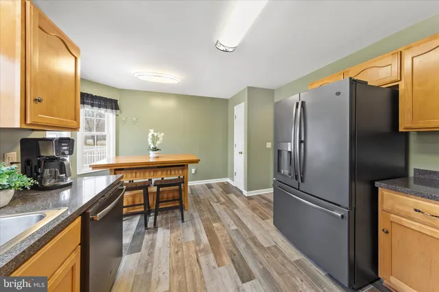 a kitchen with stainless steel appliances granite countertop a refrigerator a stove a sink a dining table and chairs with wooden floor