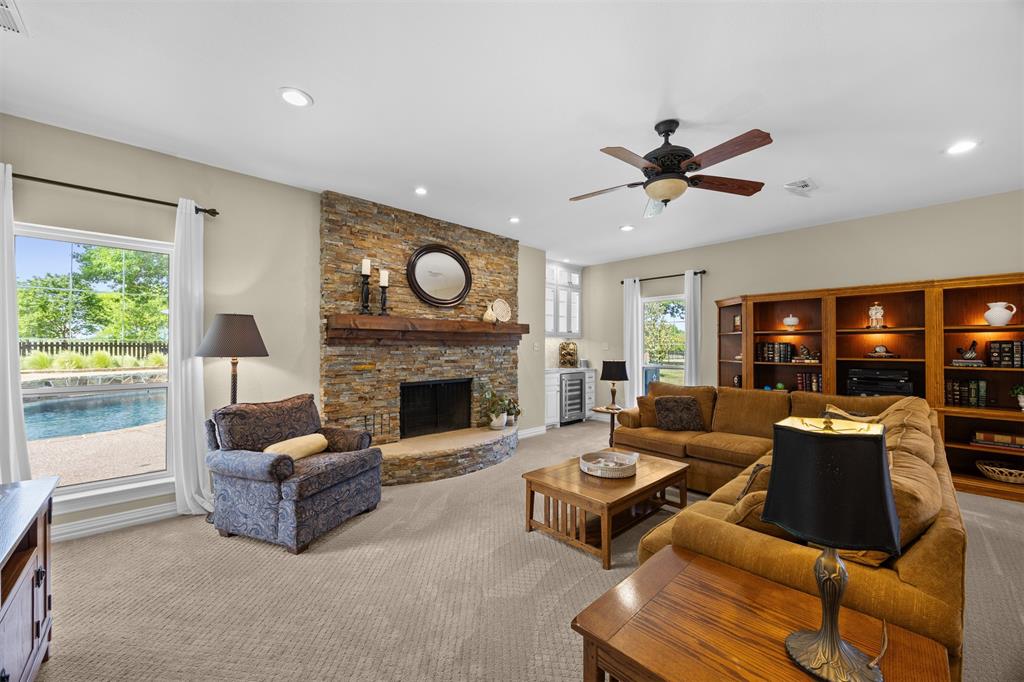 7225 Moss Ridge Road Parker, TX 75098 - Photo 7 of 40 Spacious living area featuring a stone fireplace, large windows with views of the swimming pool, built-in wooden shelving, and a ceiling fan