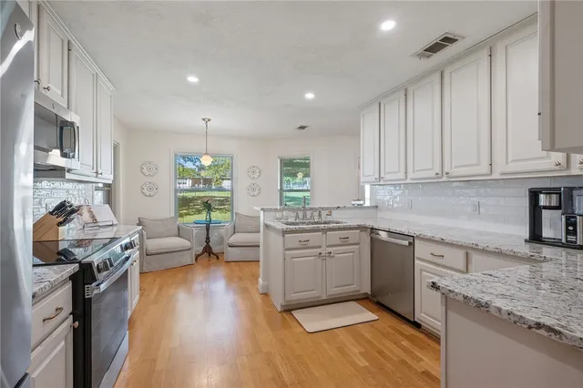 a kitchen with stainless steel appliances granite countertop a stove top oven a sink dishwasher and white cabinets with wooden floor