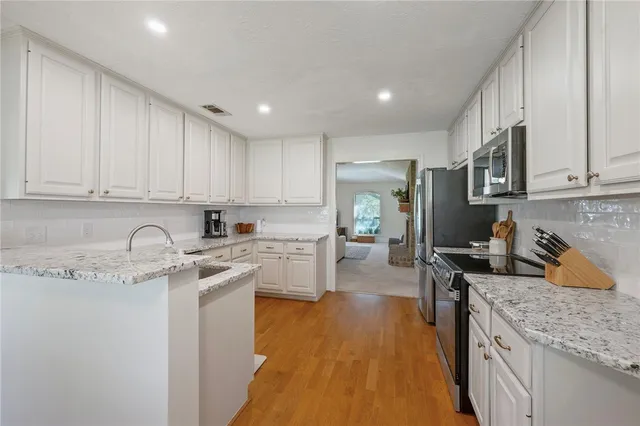 a kitchen with stainless steel appliances granite countertop a stove top oven a sink a refrigerator and white cabinets with wooden floor