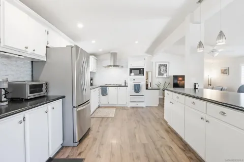 a large kitchen with stainless steel appliances kitchen island granite countertop a refrigerator a sink dishwasher a stove and white cabinets with wooden floor