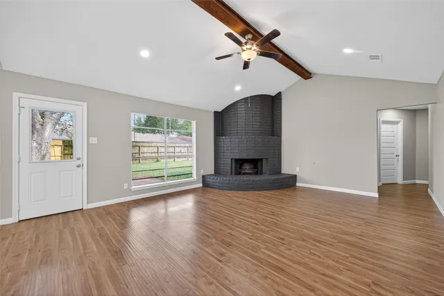 an empty room with wooden floor fireplace and windows