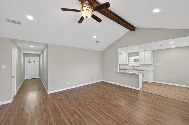 a view of an empty room and kitchen with wooden floor