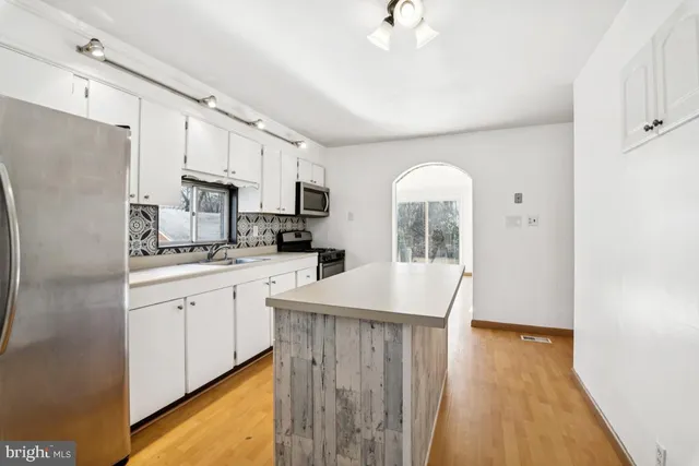 a kitchen with kitchen island granite countertop a stove a sink a refrigerator and white cabinets with wooden floor