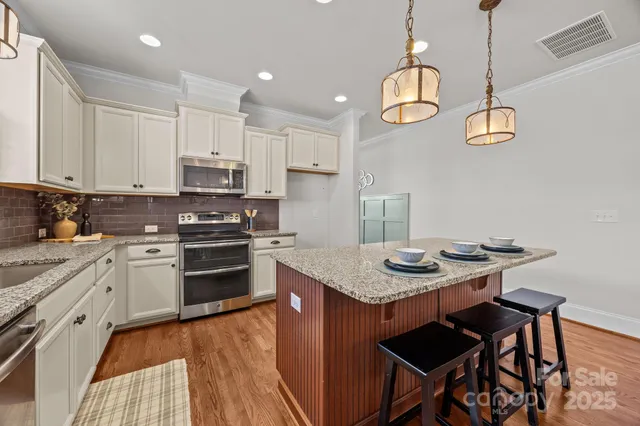 a kitchen with stainless steel appliances granite countertop a stove a sink dishwasher and white cabinets with wooden floor