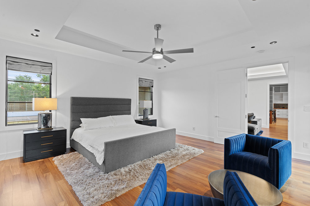 1905 Paisano Road Austin, TX 78746 - Photo 20 of 40 Natural light illuminates rich hardwood flooring in this spacious primary bedroom, featuring a contemporary ceiling fan.