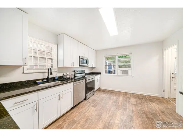 a kitchen with granite countertop a stove a sink dishwasher and white cabinets with wooden floor