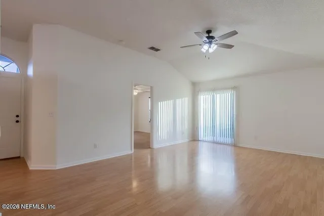 a view of an empty room with wooden floor and a ceiling fan