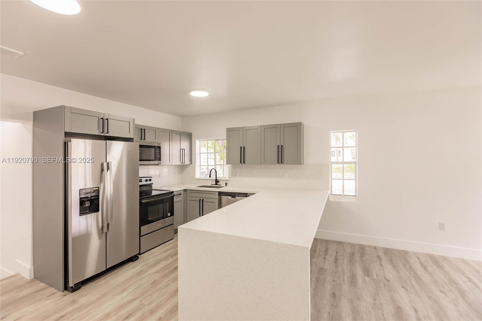 3180 Northwest 2nd Street Miami, FL 33125 - Photo 8 of 29 a kitchen with refrigerator a microwave a stove and white cabinets with wooden floor