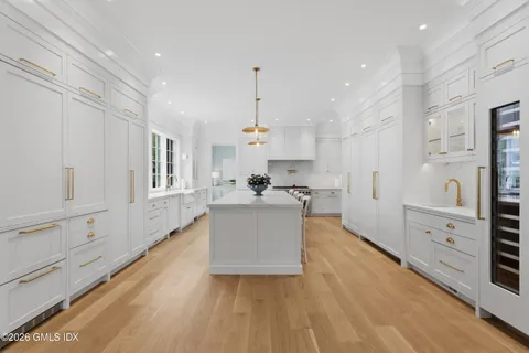 a large kitchen with kitchen island a stove a refrigerator a sink dishwasher and white cabinets with wooden floor
