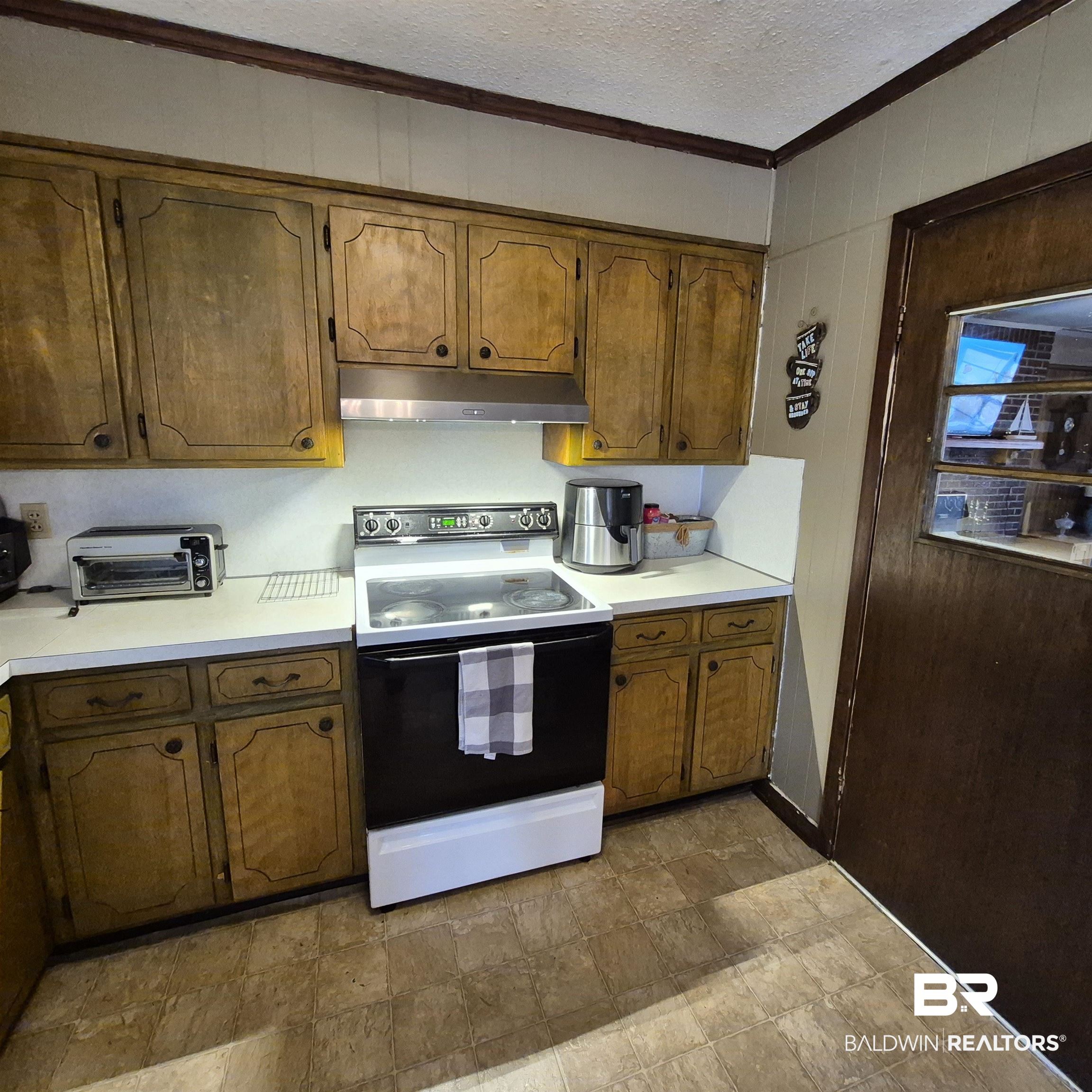 491 Forrest Avenue Castleberry, AL 36432 - Photo 9 of 33 Kitchen featuring range with electric stovetop, light countertops, stone finish flooring, a textured ceiling, and brown cabinetry