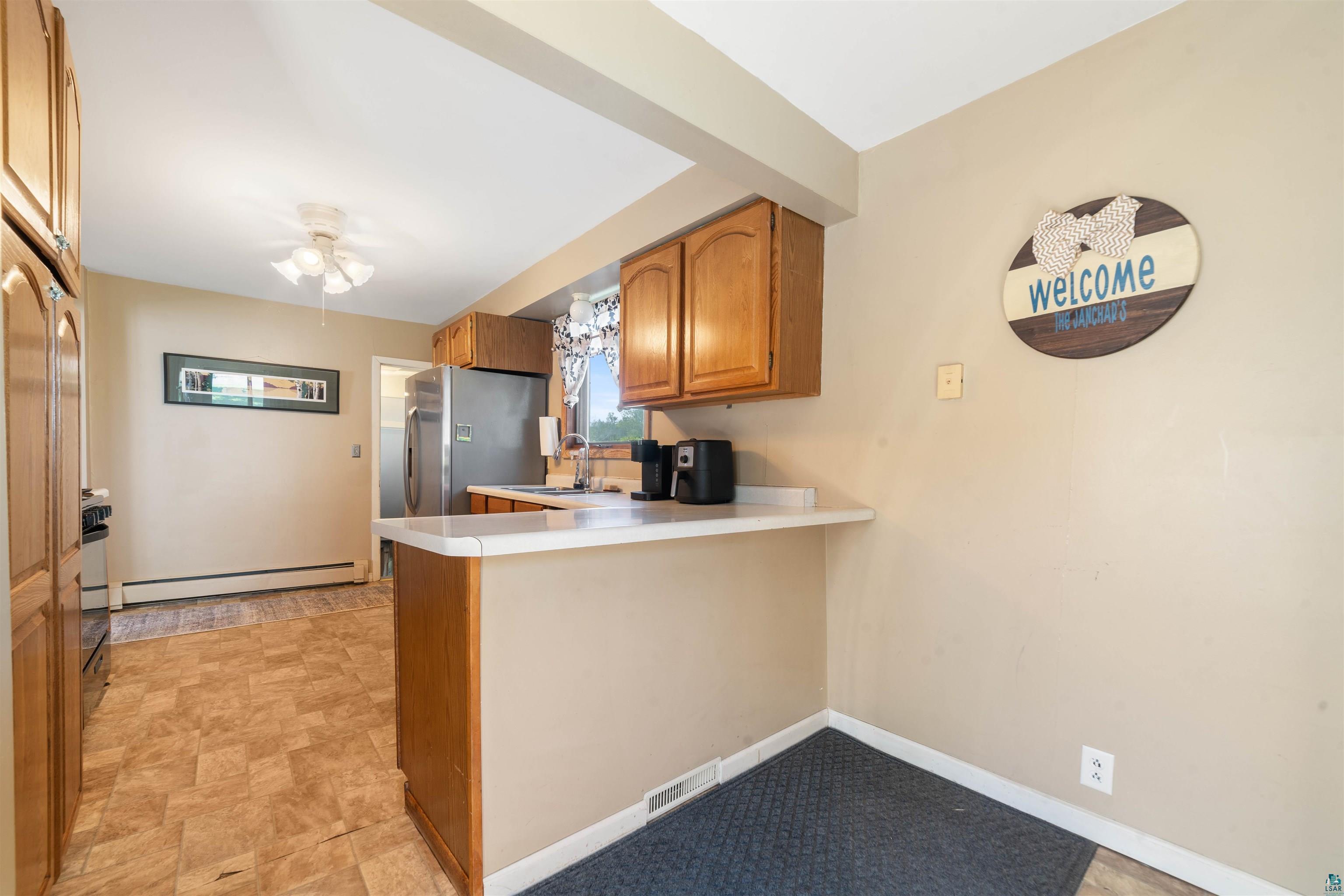 837 5th Street Proctor, MN 55810 - Photo 8 of 23 Kitchen featuring kitchen peninsula, a baseboard heating unit, stainless steel fridge, sink, and light tile floors