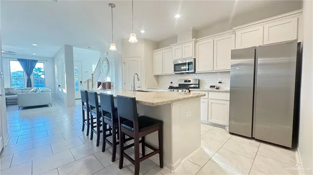 a kitchen with stainless steel appliances a refrigerator a stove a sink a dining table and chairs with white cabinets