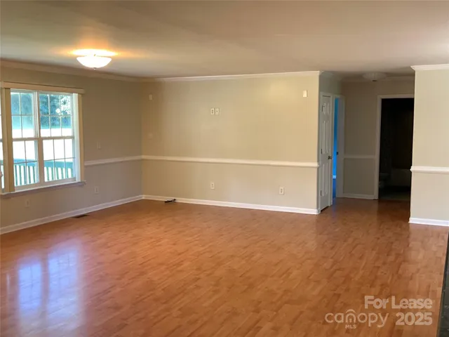 an empty room with wooden floor and windows with curtains
