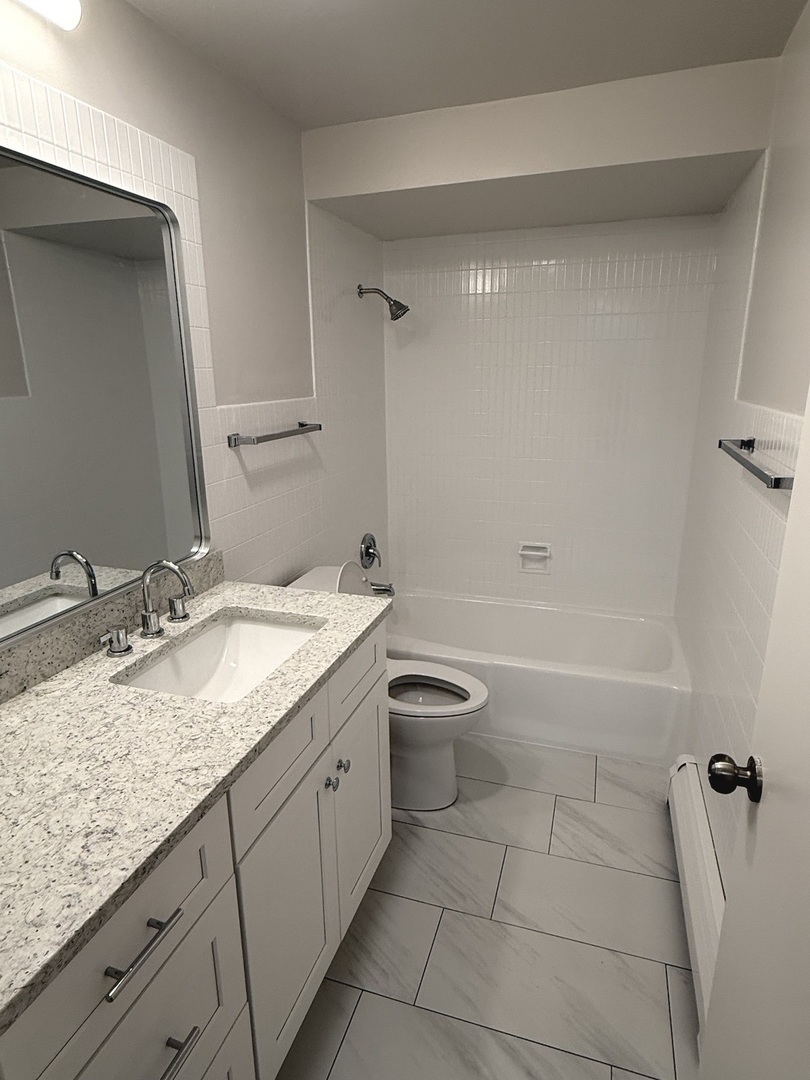8304 W Forest, Unit 3W Chicago, IL 60634 - Photo 7 of 8 a bathroom with a granite countertop sink a toilet and bathtub