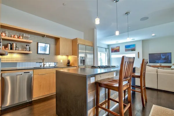 a kitchen with stainless steel appliances granite countertop a stove a sink a refrigerator a dining table and chairs with wooden floor