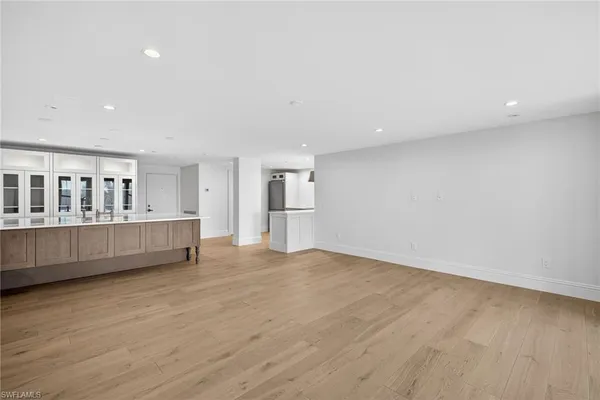 a view of an empty room with wooden floor and a kitchen