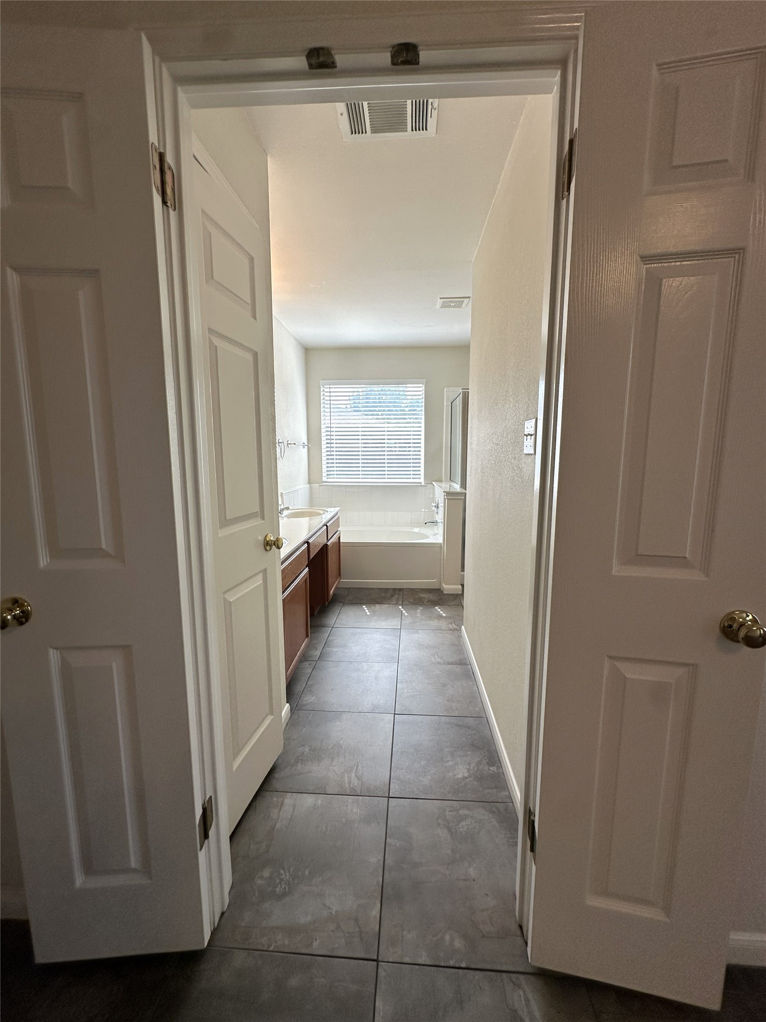 722 Ranier Lane Round Rock, TX 78665 - Photo 8 of 24 Double doors open to a spacious primary bathroom featuring large tile flooring and a soaking tub.