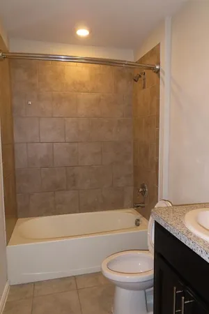 a bathroom with a granite countertop bathtub shower sink vanity and toilet