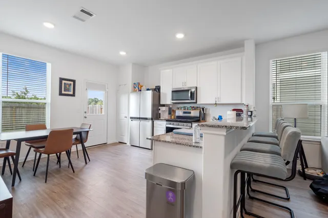 a living room with stainless steel appliances furniture a dining table wooden floor and a window