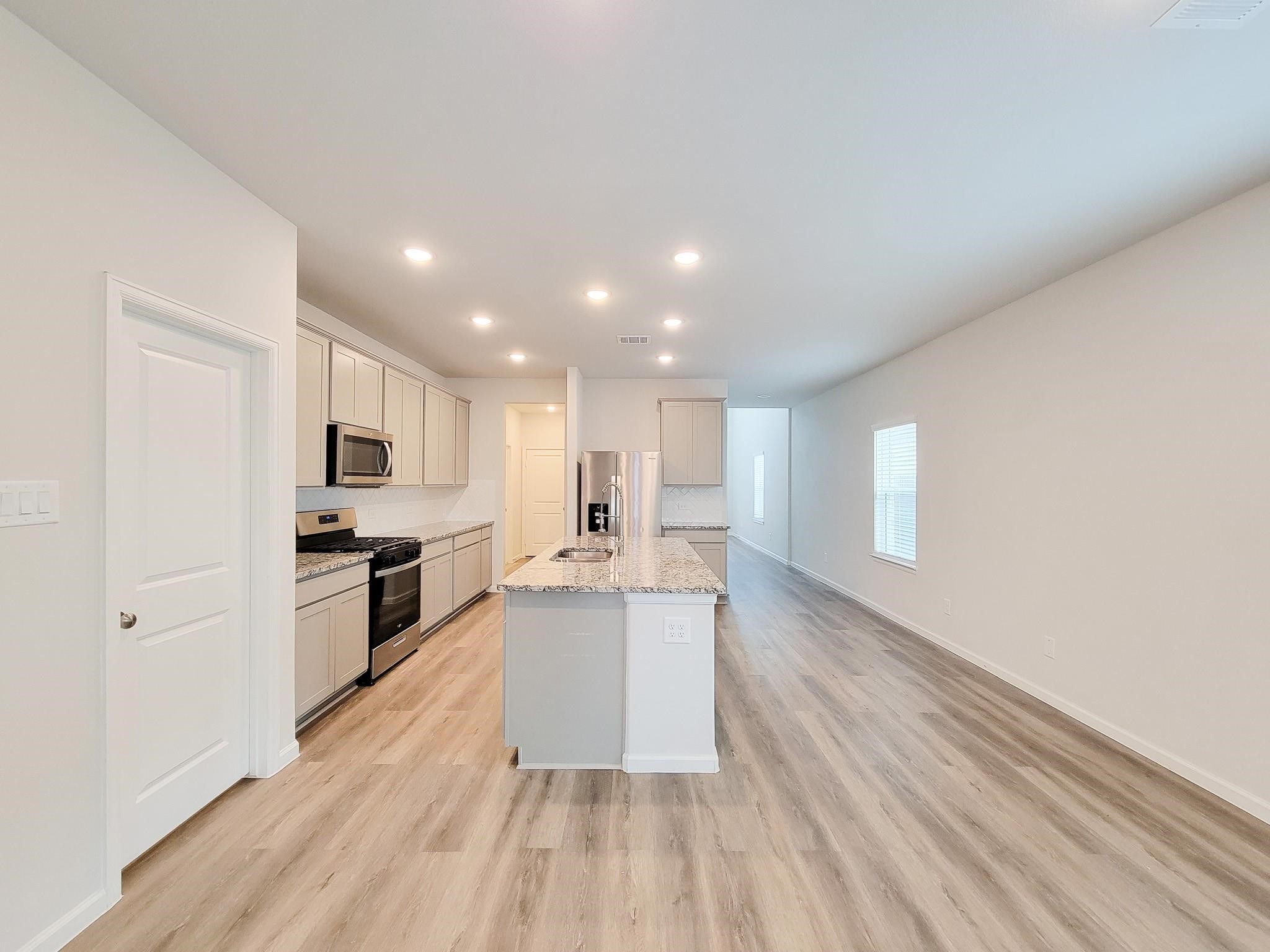 94 Valiant Ridge Trail Magnolia, TX 77354 - Photo 10 of 47 a large kitchen with kitchen island a sink dishwasher stove and white cabinets with wooden floor