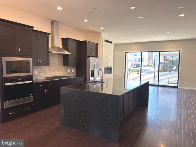 a kitchen with stainless steel appliances granite countertop a refrigerator a sink dishwasher a oven and a dining table with wooden floor