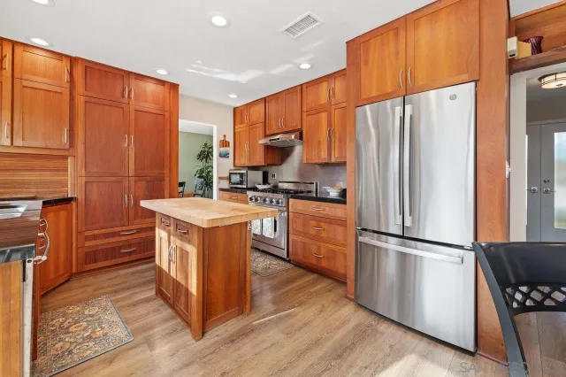 a kitchen with stainless steel appliances granite countertop a refrigerator a sink dishwasher a stove with wooden cabinets and wooden floor