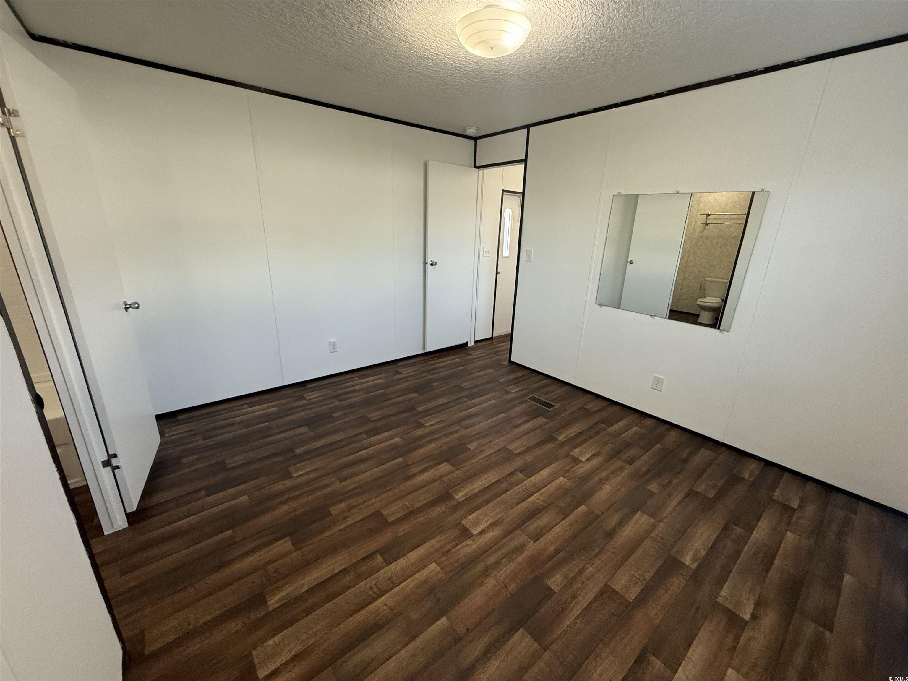 380 Hangar Court Myrtle Beach, SC 29577 - Photo 9 of 16 Unfurnished bedroom featuring a textured ceiling, dark wood-style floors, a closet, and a decorative wall