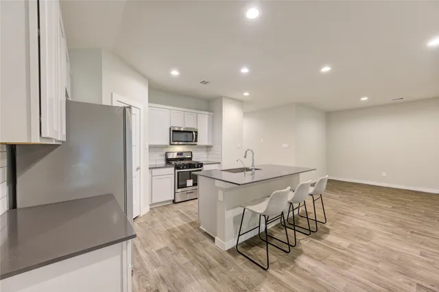 a kitchen with stainless steel appliances a microwave a stove a sink a refrigerator and chairs