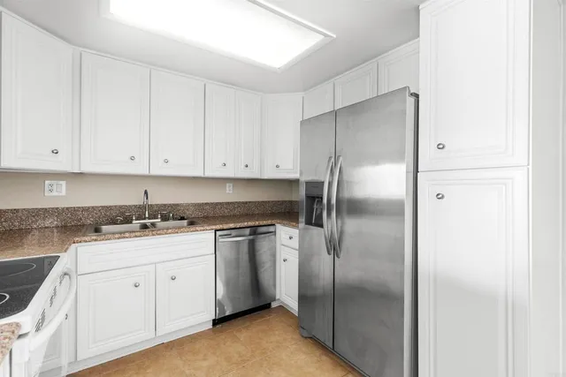 a kitchen with stainless steel appliances granite countertop a refrigerator a sink and white cabinets