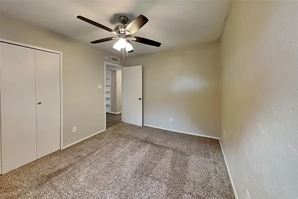 an empty room with a chandelier fan and closet