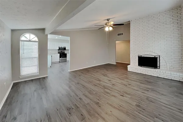 an empty room with wooden floor a ceiling fan window and fireplace